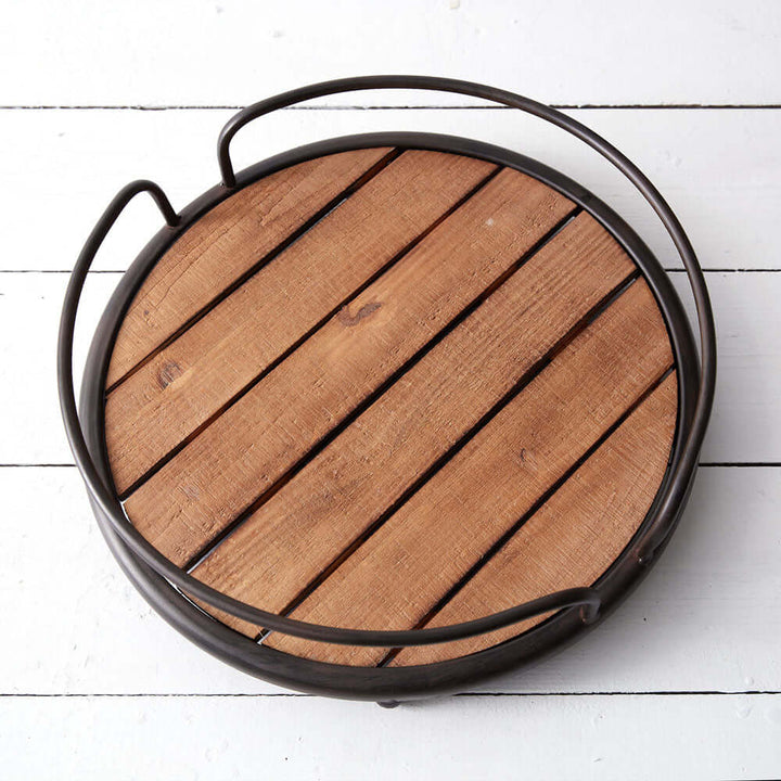 Rustic round wood tray with black metal handles, showcasing natural wood slats and vintage charm on a white surface.
