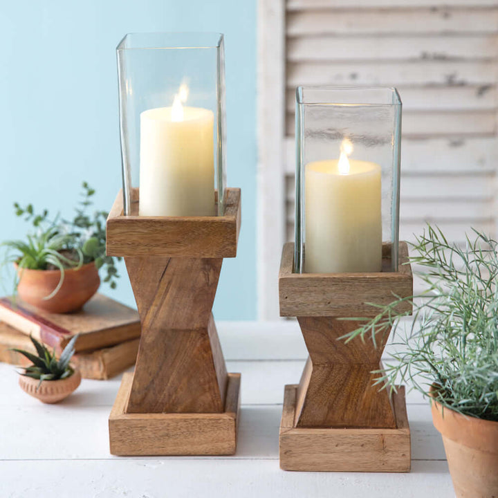 Rustic wood candle holders with glass chimneys, featuring lit candles, ideal for vintage home decor.