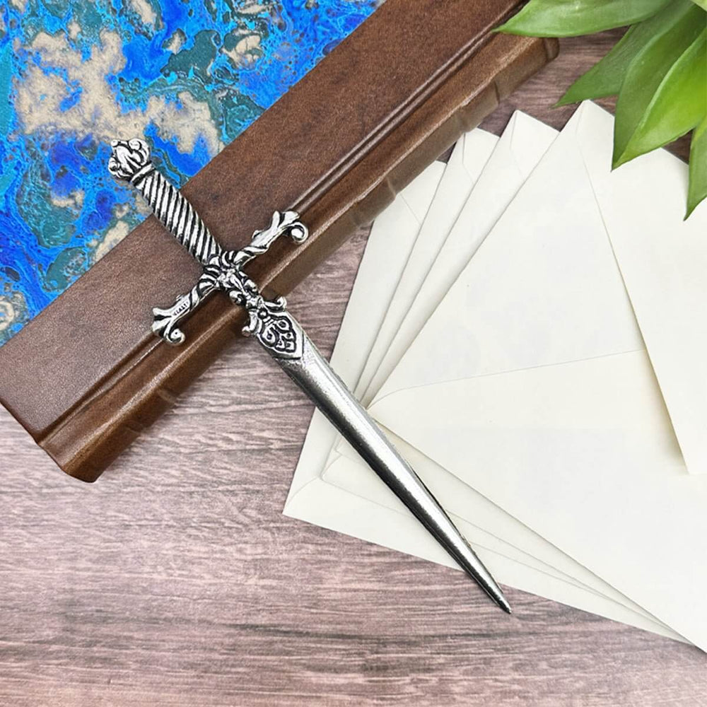 Decorative letter opener with a sword design on a wooden stand next to white envelopes.