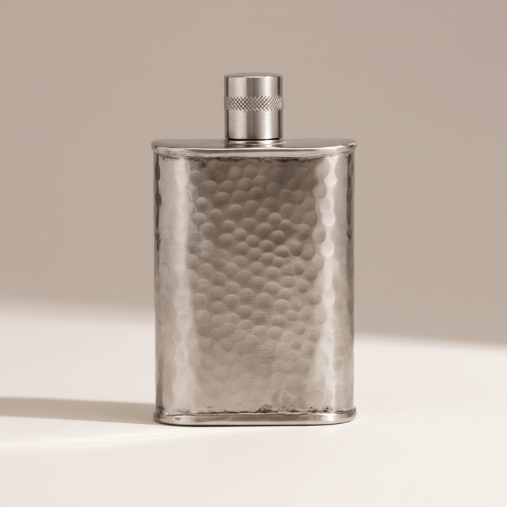 Silver flask with hammered texture on a beige background