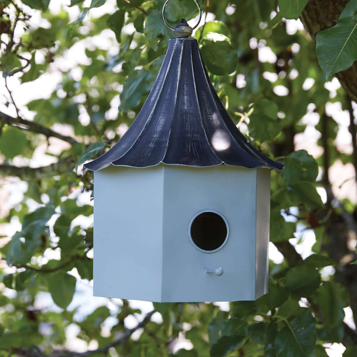 Victorian birdhouse with distressed metal roof hanging in a tree, showcasing ornate 19th-century charm.