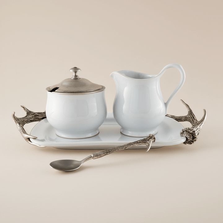 White ceramic sugar bowl, creamer, and tray with silver antler accents on a beige background