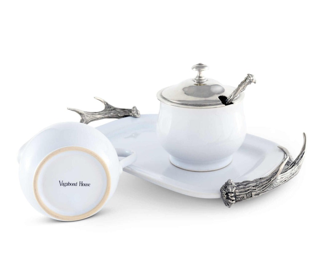 White ceramic creamer set with silver lid and handle on a white tray with decorative elements.