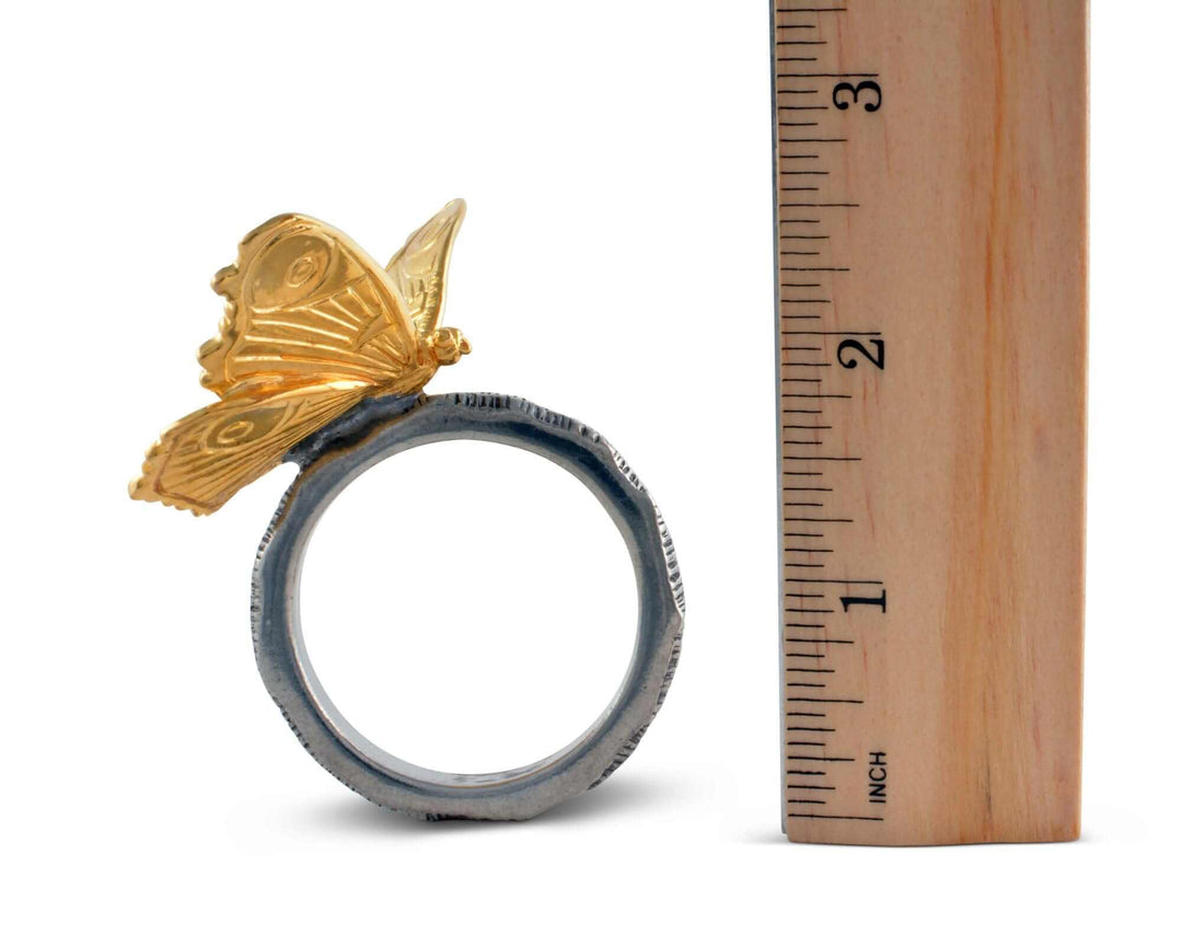 Gold butterfly ring on a white background with a wooden ruler for scale.
