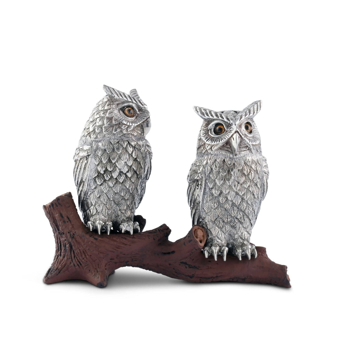 Two silver owl figurines on a wooden branch against a white background