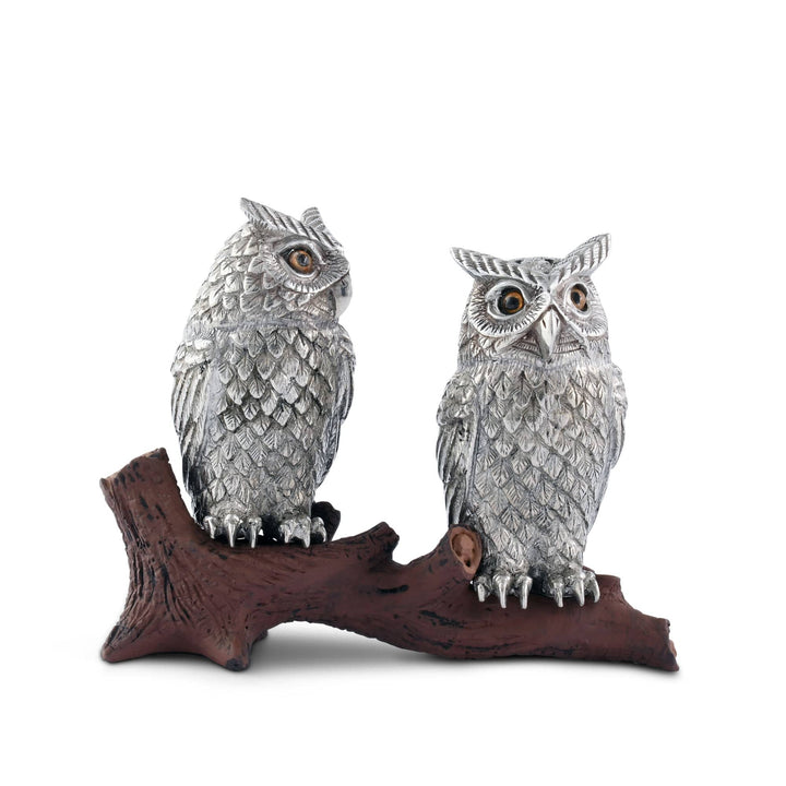 Two silver owl figurines on a wooden branch against a white background
