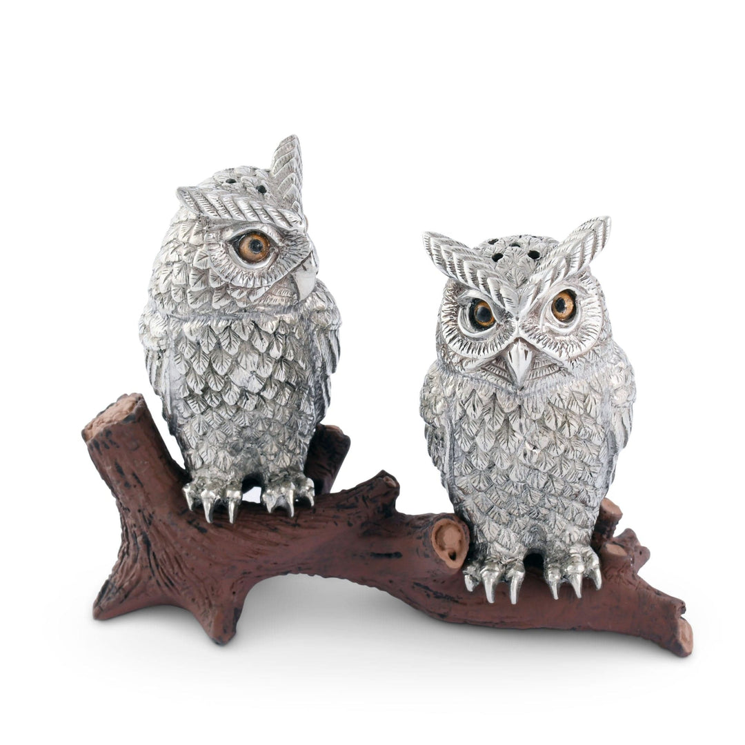 Two silver owl figurines on a wooden branch against a white background