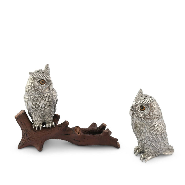 Two silver owl figurines on a wooden branch and stand against a white background