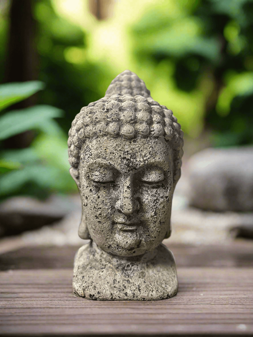 Vintage Buddha head statue with weathered texture, symbolizing spiritual wisdom and peace in a serene garden setting.