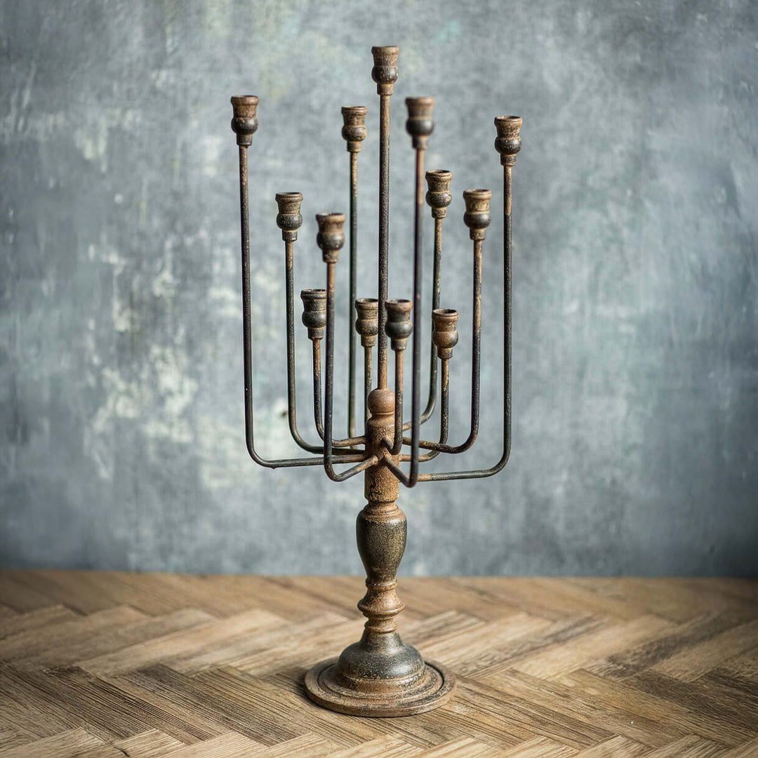 Vintage-style metal candelabrum on a wooden surface with a textured gray wall background