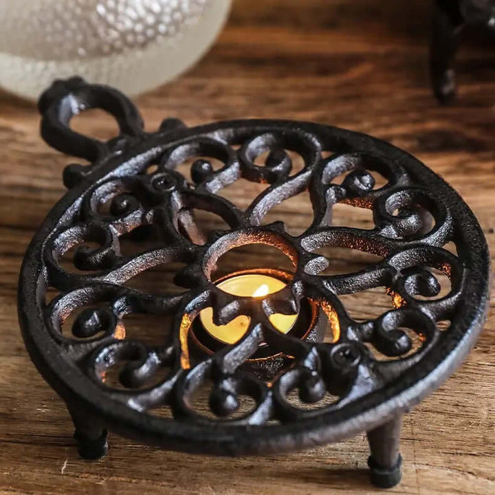 Vintage cast iron teapot warmer with ornate handle, featuring intricate design and lit candle.