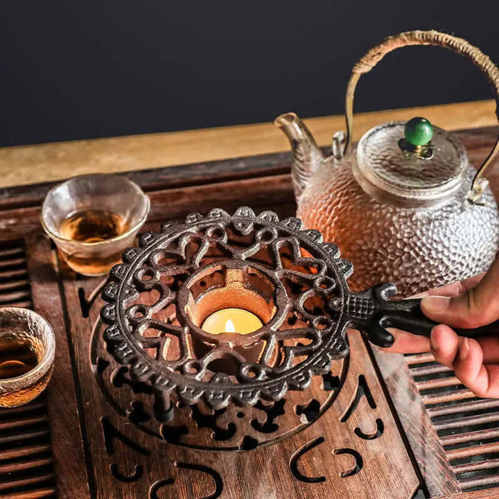 Vintage cast iron teapot warmer with ornate handle, keeping tea warm on a wooden tea tray with glasses.