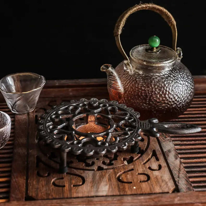 Vintage cast iron teapot warmer with ornate handle, enhancing tea-drinking rituals on a wooden tea set.