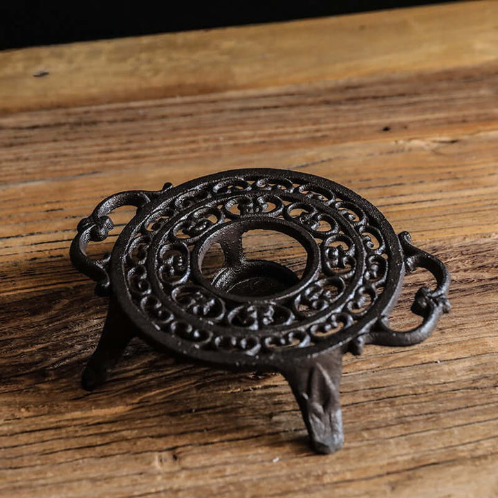 Decorative black metal trivet with intricate design on a wooden surface