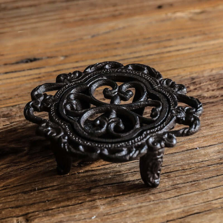 Decorative black metal trivet on a wooden surface