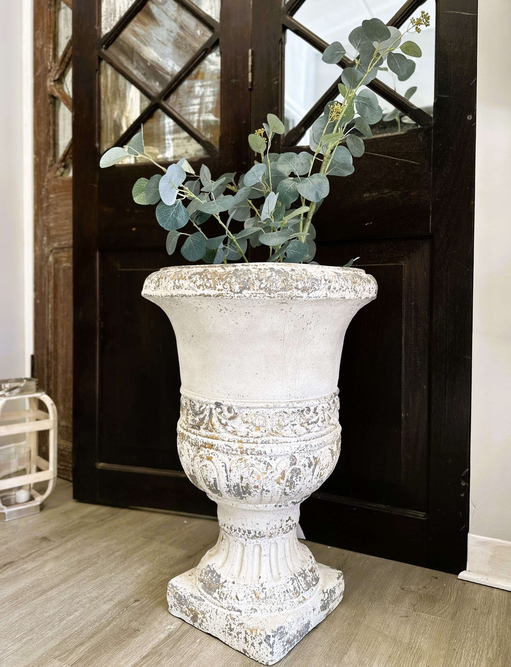 Vintage distressed decorative urn planter with eucalyptus, adding rustic charm to indoor decor.