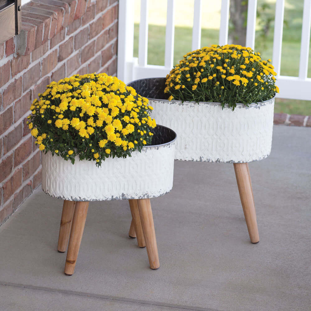 Vintage embossed metal planters with wood legs holding yellow flowers, perfect for rustic farmhouse decor.