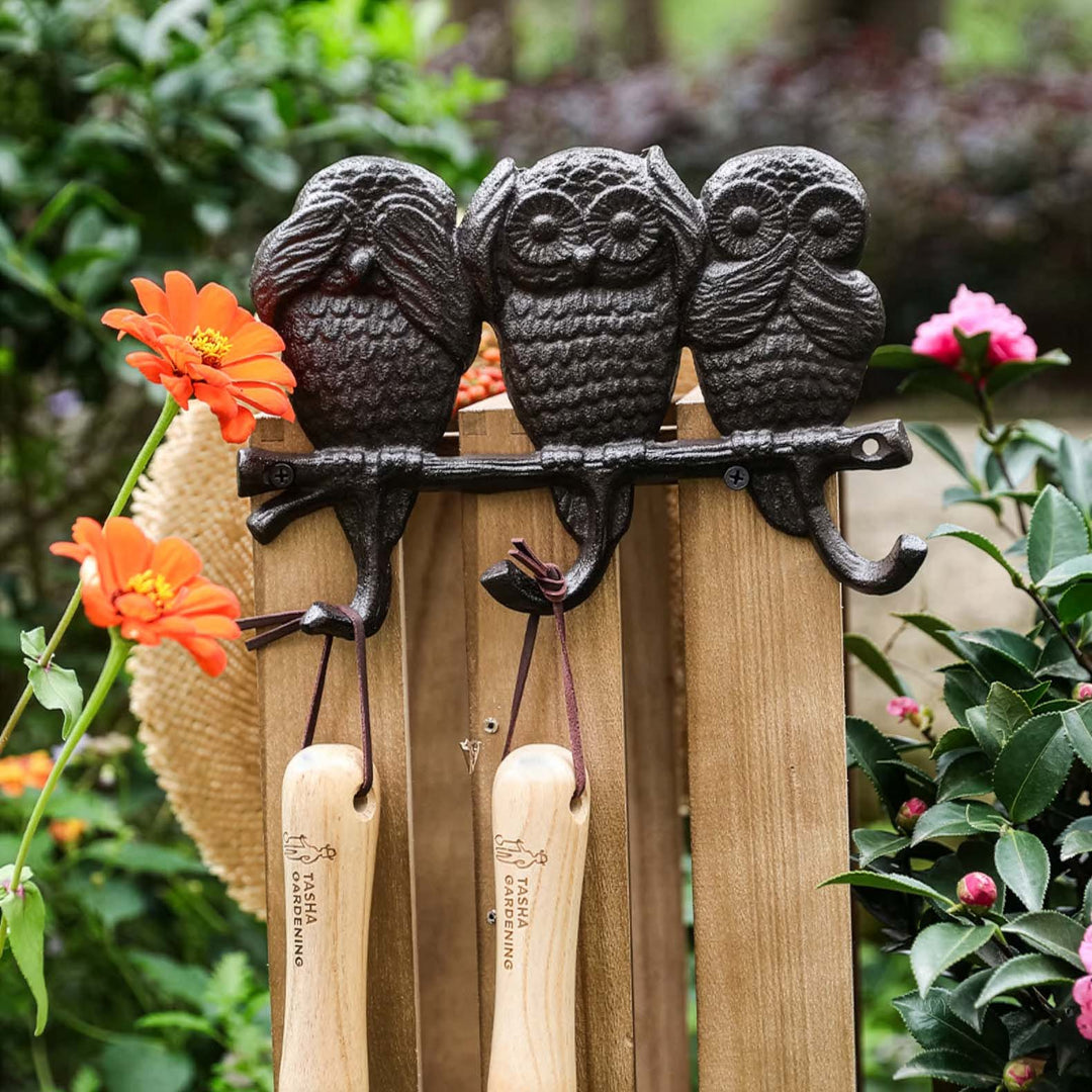 Decorative owl-shaped tool holder with gardening tools against a garden background