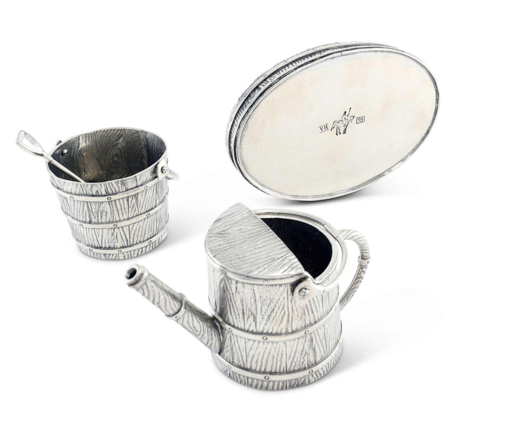 Metal creamer set including a watering can, bucket, and spade on a white background.