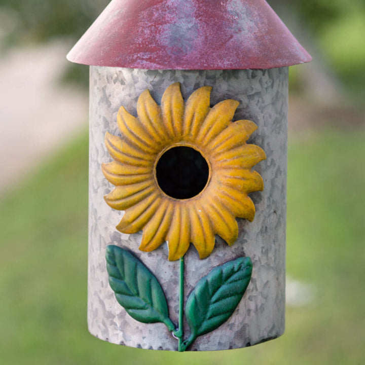 Vintage farmhouse sunflower birdhouse with cheerful sunflower design against a blurred green garden background.