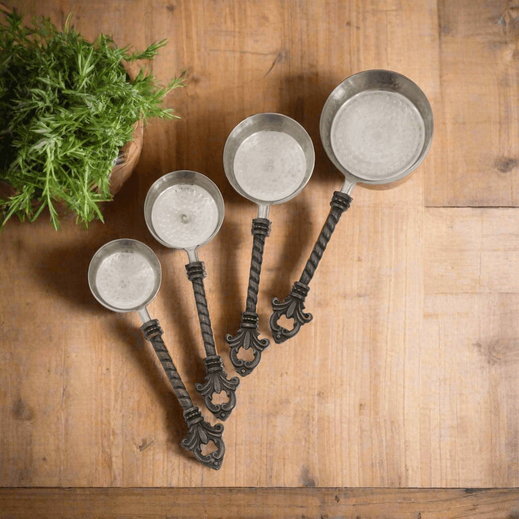 Set of four decorative measuring cups with ornate handles on a wooden surface.