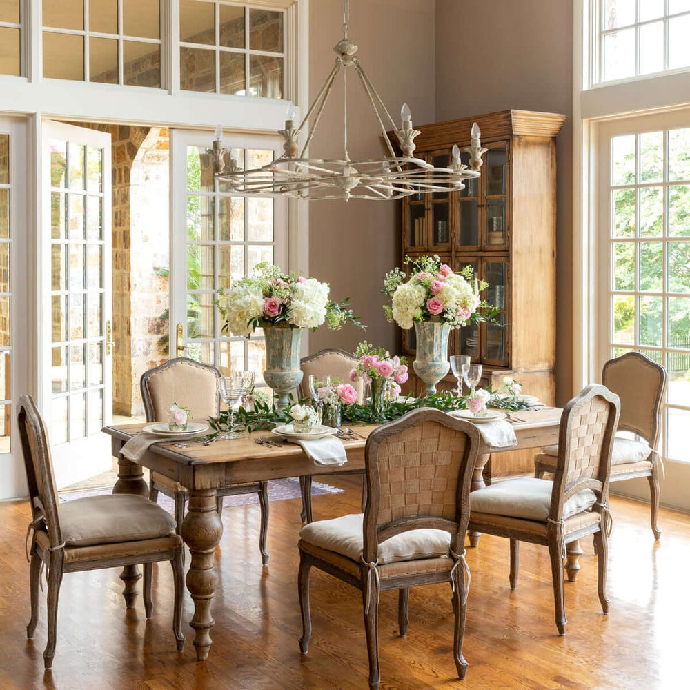 Dining room with wooden table and chairs, floral centerpieces, and large windows.