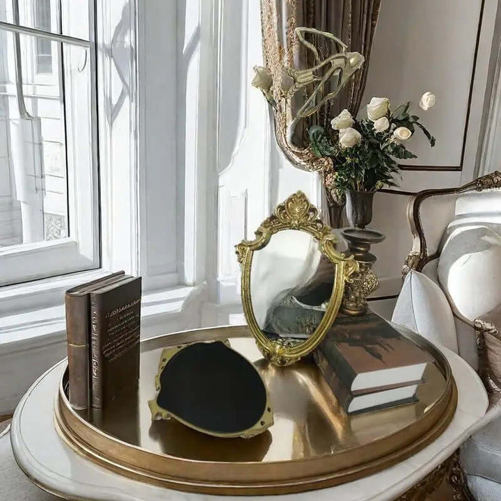 Vintage gold vanity wall mirror with Baroque frame, elegant decor on a stylish table with books and flowers.