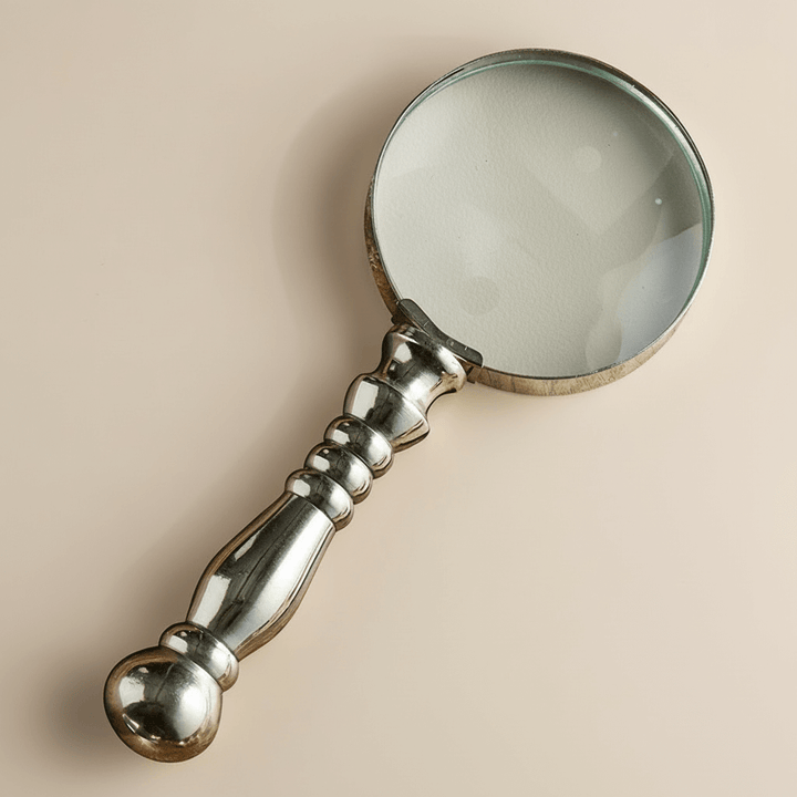 Vintage-style magnifying glass with a decorative handle on a beige background