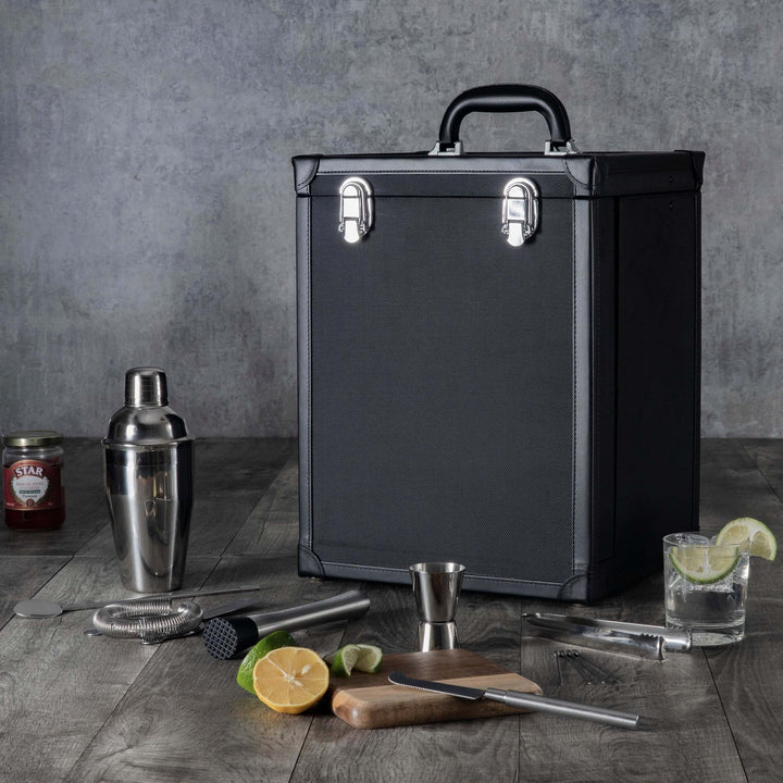 Black cocktail kit with bar tools on a wooden surface against a gray background