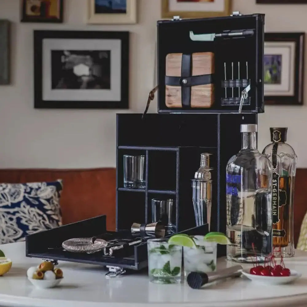 Bartender kit with bottles and glasses on a table with framed pictures in the background