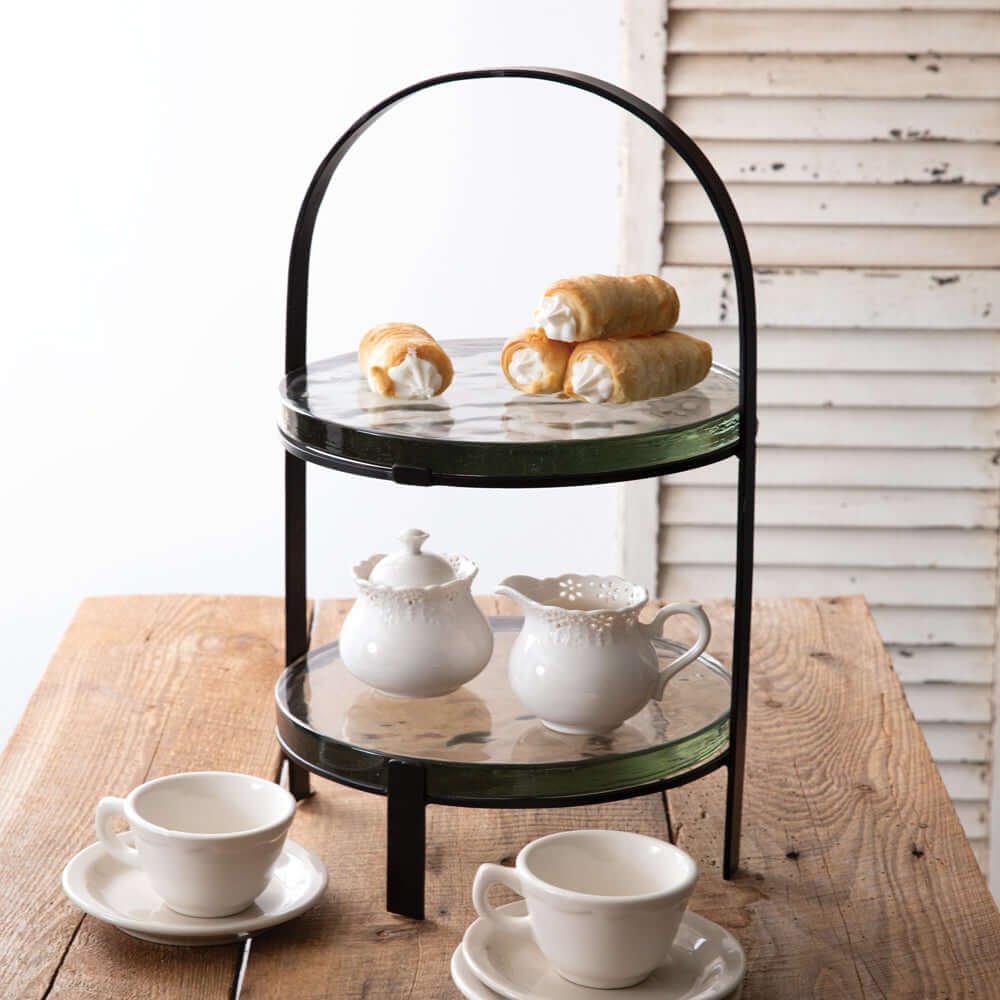 Two-tiered serving tray with tea set and pastries on a wooden table.