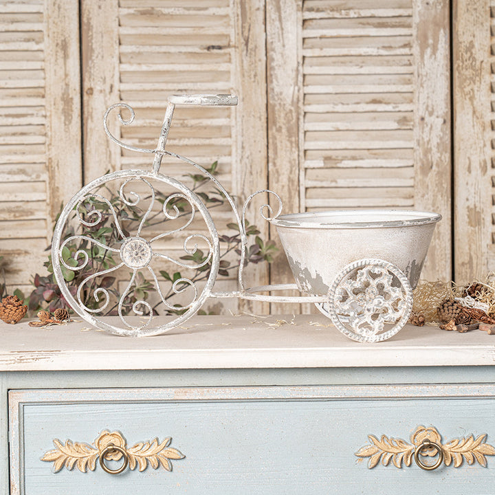 Decorative metal tricycle planter on a wooden surface with a rustic background