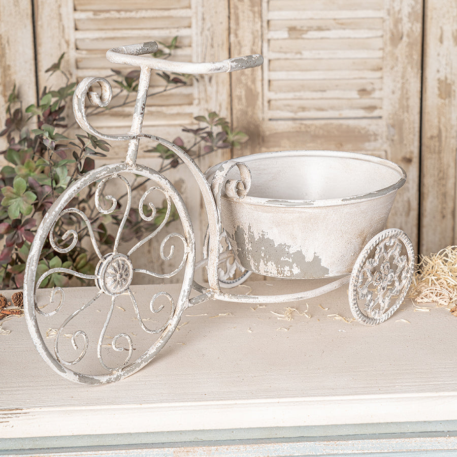 Decorative white metal tricycle with a basket on a wooden surface.