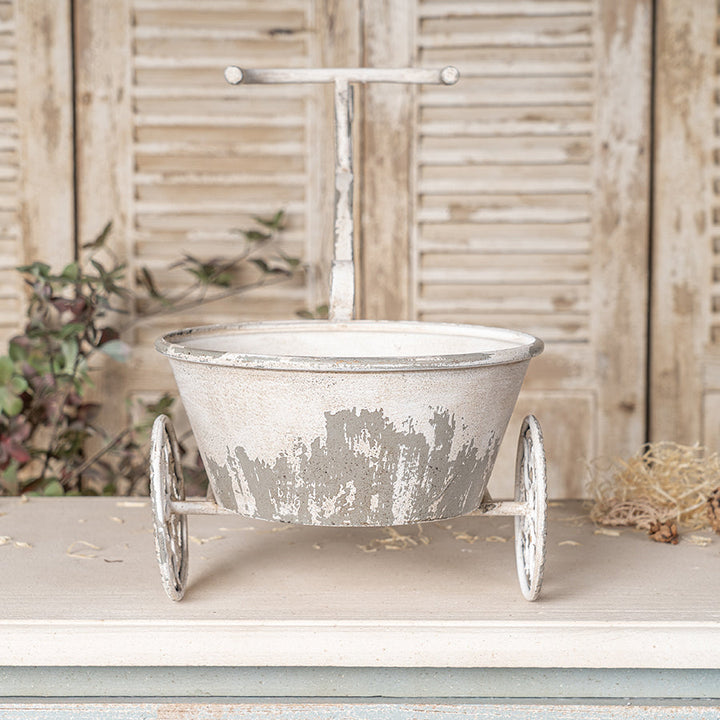 Decorative metal planter with wheels on a wooden surface with a rustic background