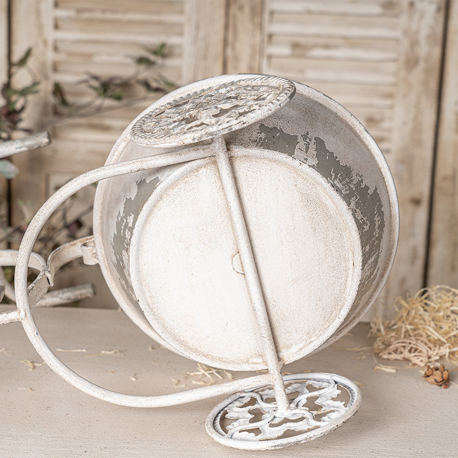 Decorative white metal planter with intricate designs on a wooden surface.