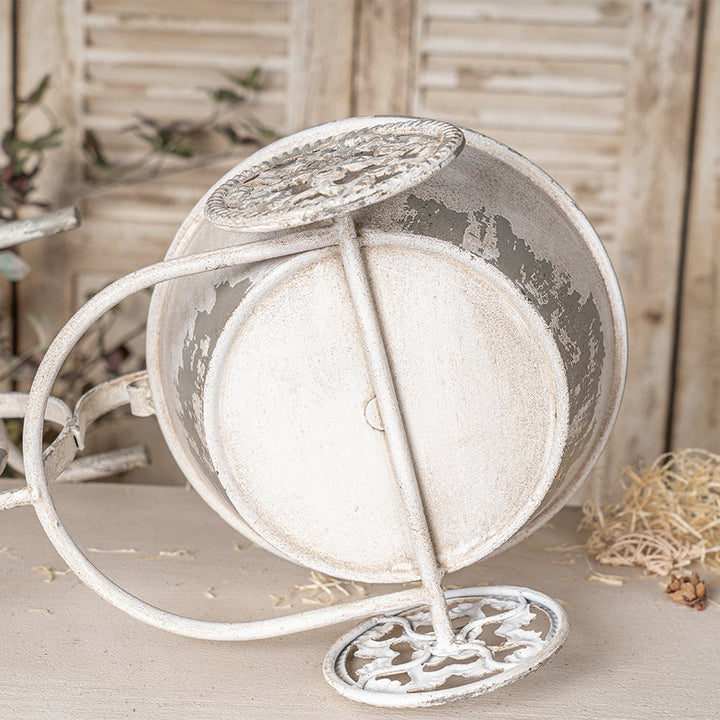 Decorative white metal planter with intricate designs on a wooden surface.