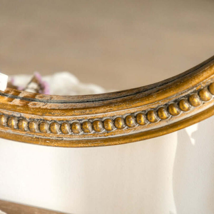 Close-up of a vintage round gold wall mirror with an ornate carved wood frame showcasing detailed beading and scrollwork.