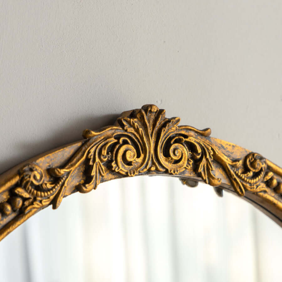 Close-up of vintage round gold wall mirror with ornate carved wood frame and European-style scrollwork design.