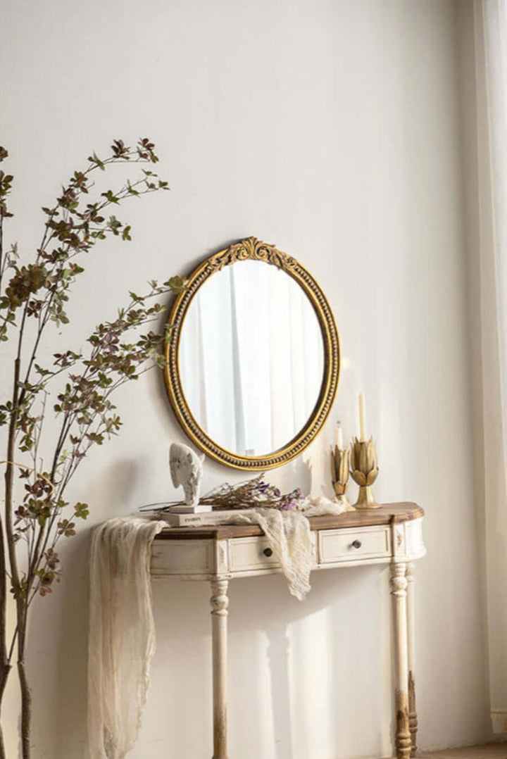 Vintage round gold mirror with ornate carved frame on antique table, elegant classic decor.