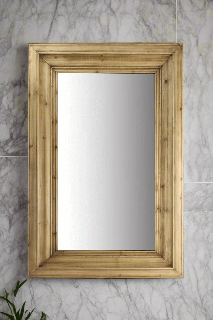 Wall mirror with molded pine frame against a marble wall, enhancing vintage-inspired decor with timeless charm.