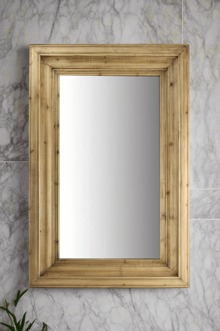 Wall mirror with molded pine frame against a marble wall, enhancing vintage-inspired decor with timeless charm.