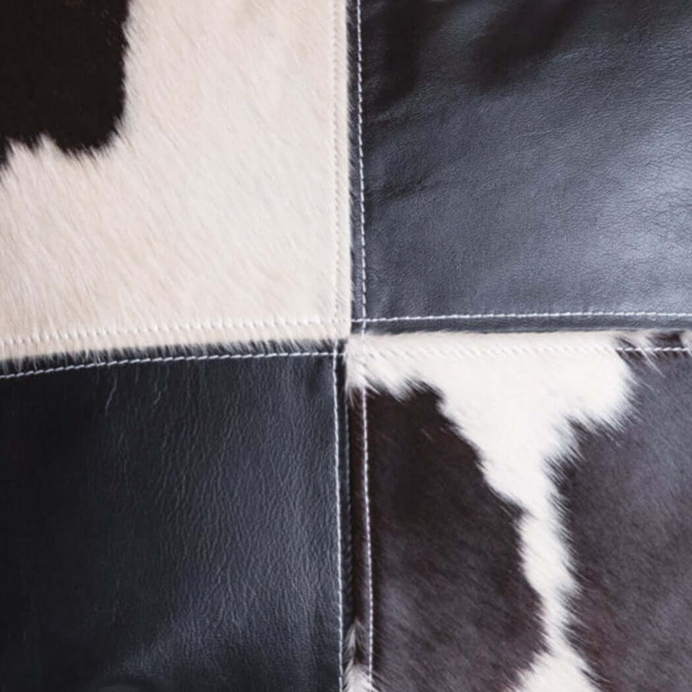 Close-up of a western cowhide and leather patchwork pillow showcasing black and white cowhide textures.