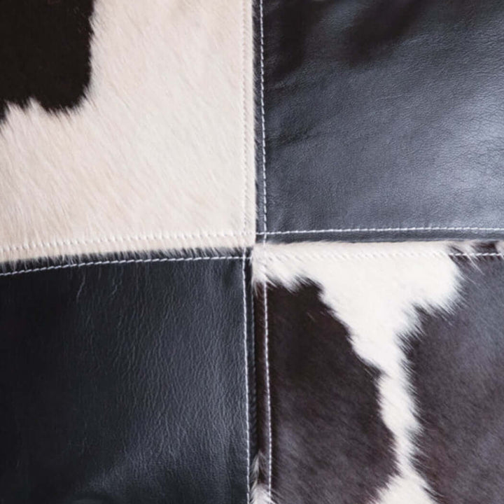 Close-up of a western cowhide and leather patchwork pillow showcasing black and white cowhide textures.