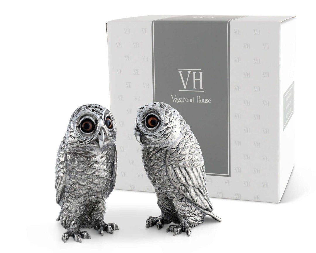 Two silver owl figurines in front of a Vagabond House box on a white background