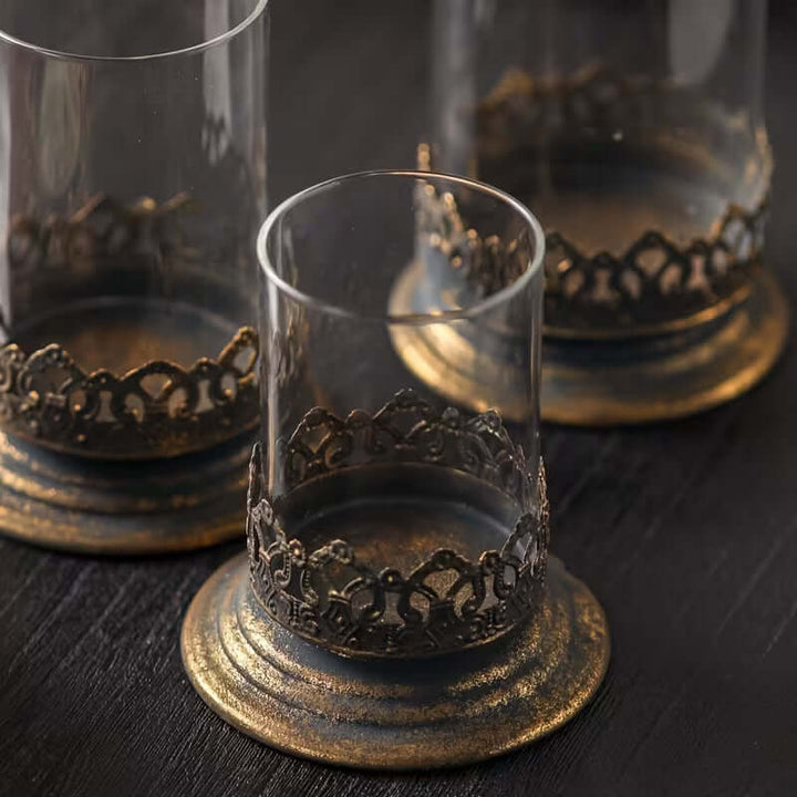 Decorative glass candle holders with ornate metal bases on a dark surface