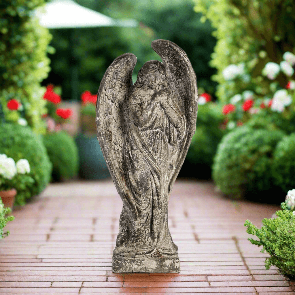 Aged Stone Italian Garden Angel Statue in lush garden with flowers, featuring a weathered patina finish and serene expression.