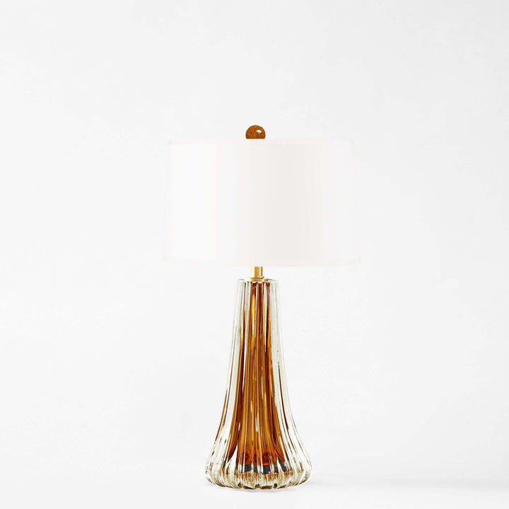 Tall, slender glass table lamp with a wide base narrowing to a pointed tip on a white background