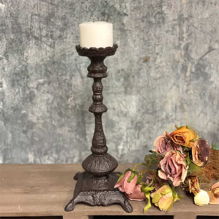 Antique cast iron candle holder with ornate details, featuring a white candle and vintage flowers in soft tones.