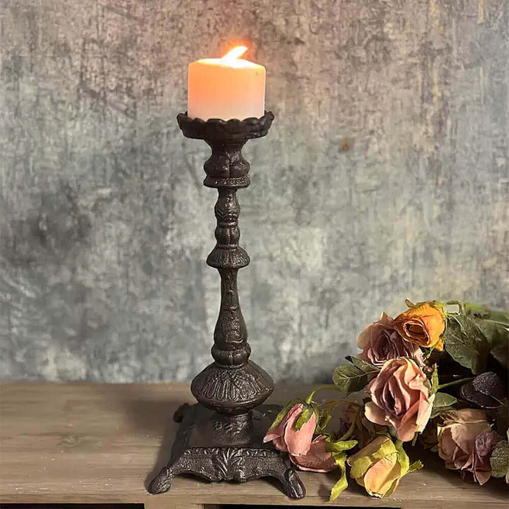 Antique cast iron candle holder with lit candle, surrounded by faded flowers, showcasing old-world elegance.