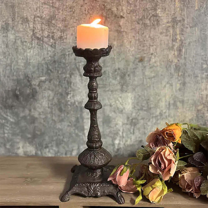 Antique cast iron candle holder with lit candle, surrounded by faded flowers, showcasing old-world elegance.